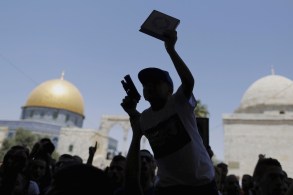 A Palestinian youth is silhouetted as he holds a toy gun and a Koran during a protest after Friday prayers on the compound in Jerusalem's Old City